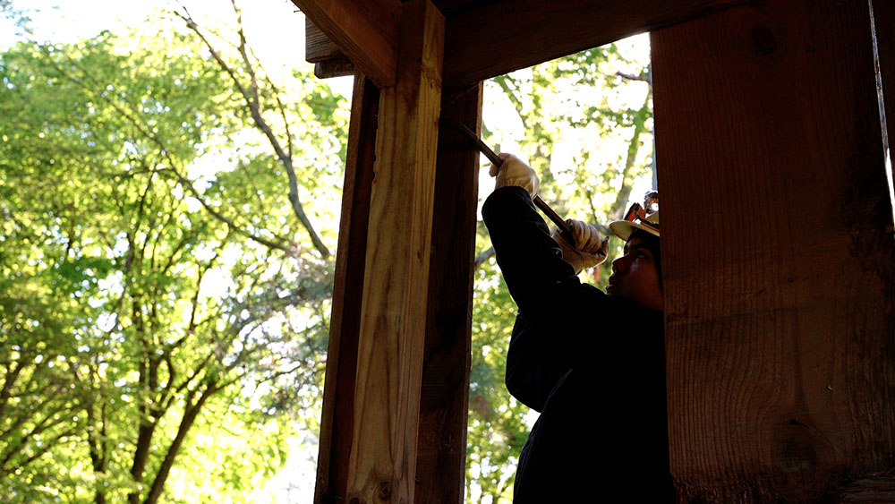 Student wearing a hard hat and using a crowbar on a deck post